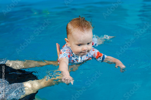 Fotografía An instructor holds an infant in water as the baby practices swimming movements