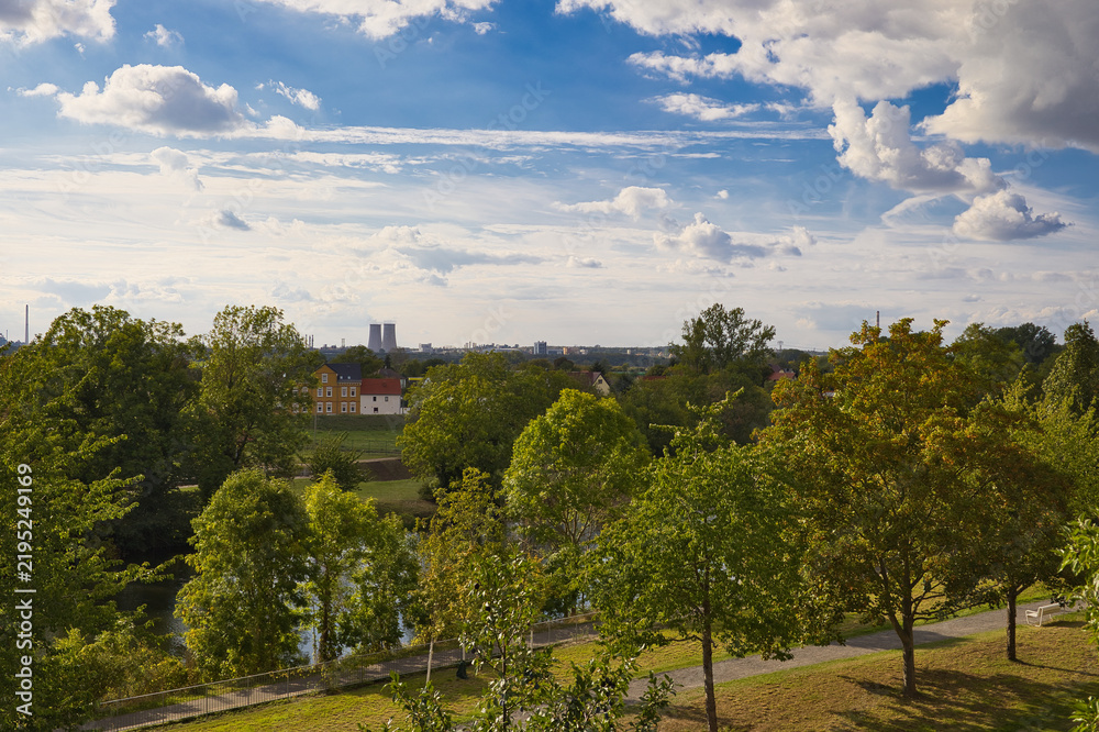 Obraz premium Weitblick vom Kurpark in Bad Dürrenberg über grüne Wiesen und Häuser auf den Chemiepark Leuna am Horizont mit bewölktem Himmel, Saalekreis, Sachsen-Anhalt, Deutschland