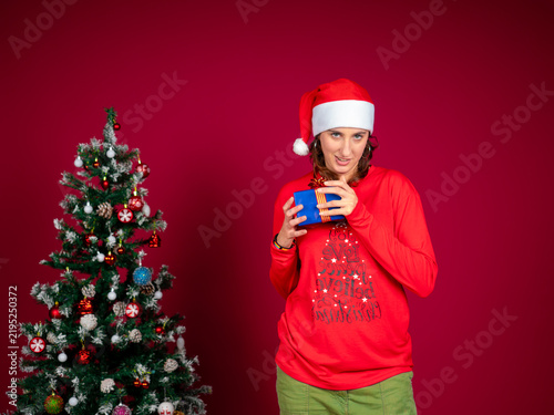 Cuadro en lienzo Woman wearing santa hat holding christmas gift looking mischievous