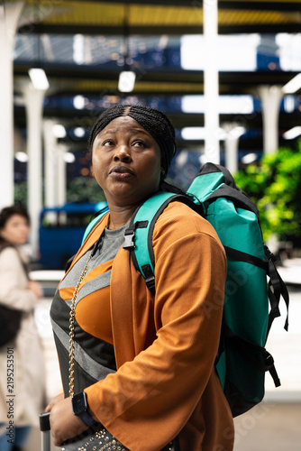 Foto Female passenger carries a backpack and pulls trolley luggage across a bus station during weekday travel, heading through the terminal before departure
