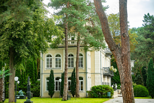 Konstancin-Jeziorna, Warsaw, Poland, 5 September 2026, Side view of the historic Villa la Fleur museum building in Konstancin-Jeziorna, Poland, set in a lush park with tall trees and statues.
