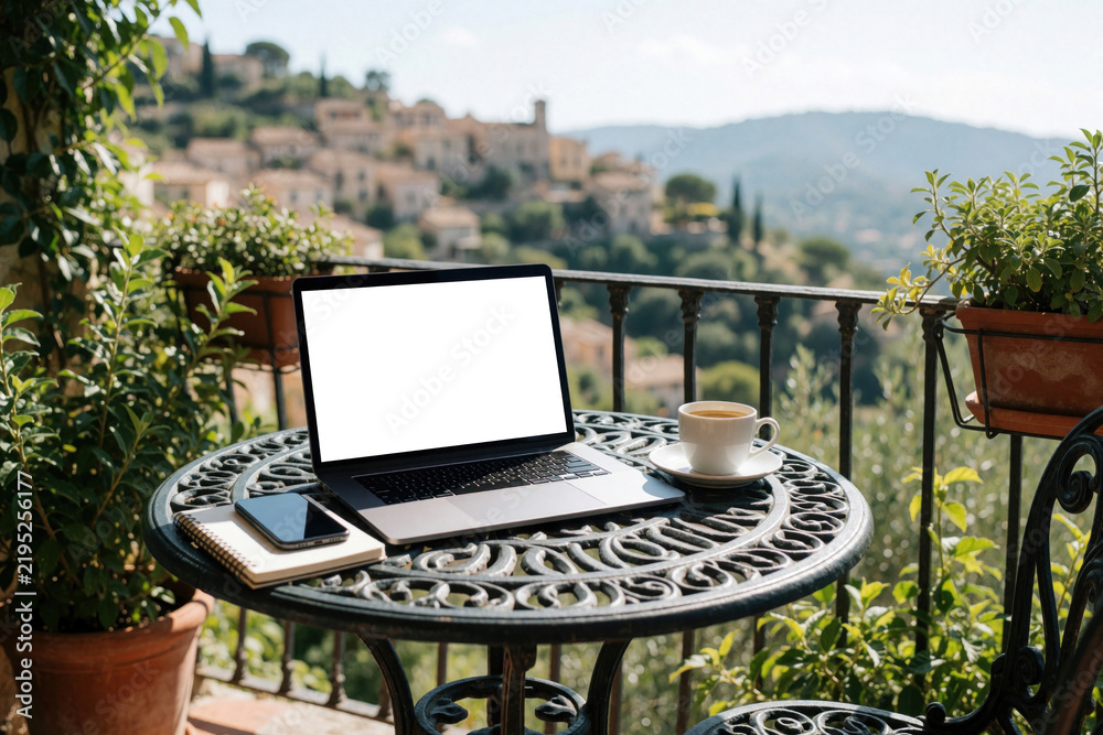 Fototapeta premium Laptop, coffee cup, and phone rest on a table on a balcony with a scenic view. This setup suggests remote work or a peaceful morning with technology.