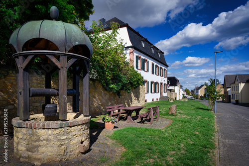 Obraz na płótnie Idyllic village square in Buervenich featuring a historic draw well, Haus Piedmo