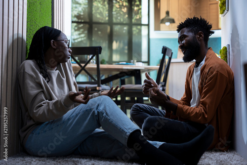 Obraz na plátne Upset Black couple lying on hallway carpet during an enraged conflict, expressing displeasure and emotional pain while depicting toxic relationship issues and domestic fighting at home