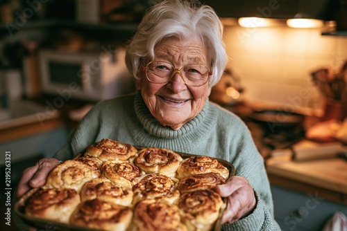 smiling elderly woman holding a baking pan of fresh homemade cinnamon rolls in the kitchen