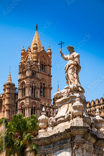 Statue of a saint with cross before Palermo Cathedral's Gothic tower, Sicily