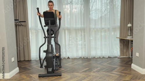 Woman performs reverse stepping on elliptical machine using moving handles. Balanced home workout engaging different muscle groups.