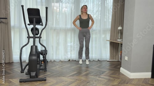 Woman in sports top and leggings marches in place lifting knees high with hands on hips. Simple home warmup exercise.