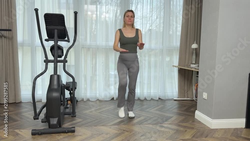 Woman in sportswear performs running with heels hitting glutes as imitation of jump rope. Dynamic home cardio exercise.