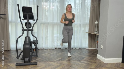 Woman in sportswear performs coordinated steps lifting knees and controlling arm movement. Balanced indoor cardio training.