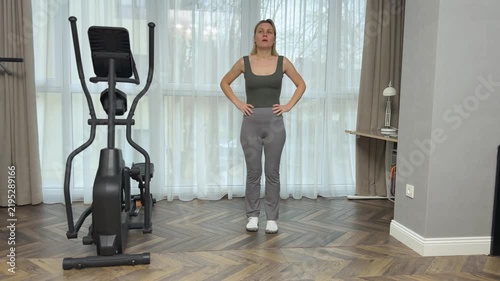 Woman in fitted sportswear jumps high vertically in living room. Home plyometric workout for power and endurance.
