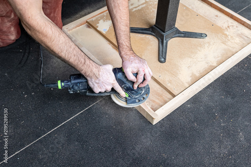 Close Up of Craftsman Sanding Wooden Table Edge with Power Sander