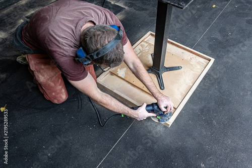Worker Sanding Underside of Wooden Table During Furniture Restoration