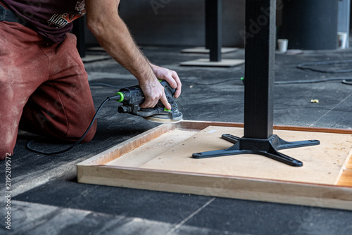 Craftsman Sanding Edge of Upside Down Wooden Table During Restoration