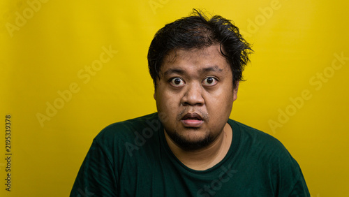 Bild auf Leinwand Young Asian male displays terrified and shocked expression with wide eyes against bright yellow backdrop