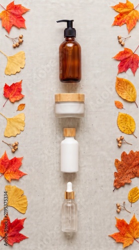 Organic skincare bottles arranged in a row with vibrant autumn leaves border on linen texture, seasonal eco friendly wellness, cosmetic flat lay mockup