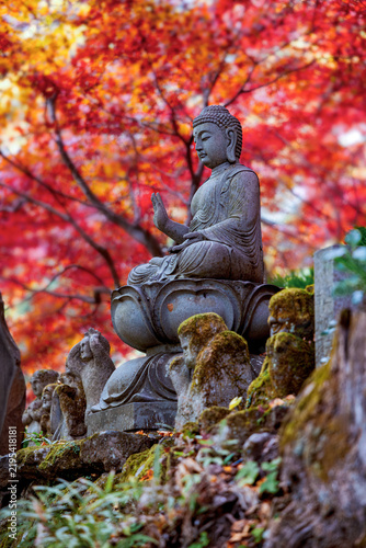 Stone Buddha statue surrounded by vivid red and orange autumn foliage