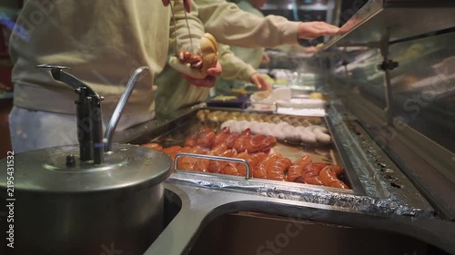 Street food at Munich Christmas fair with traditional German sausages. Chef hands preparing bratwurst, weisswurst, and currywurst in buns. Evening lights enhance festive mood.