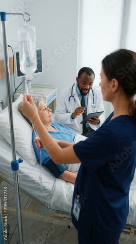 Caring Medical Professionals Attending To Patient Receiving Intravenous Therapy In Hospital Room