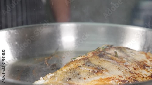 Close-up of golden fish fillet frying in stainless steel pan with oil. Crispy skin, rising steam, professional kitchen cooking process, delicious seafood meal preparation Slow motion 4k video