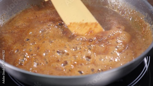 Thick caramel bubbling in saucepan while wooden spatula stirs. Golden brown sweet mass cooking on stove, professional confectionery process, homemade dessert preparation Slow motion 4k video