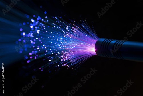 Fiber optic cable emitting glowing blue and purple light beams in dark space