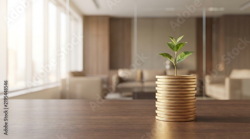 A small green plant sprouts from a stack of gold coins on a wooden table in a modern office, symbolizing financial growth and investment.