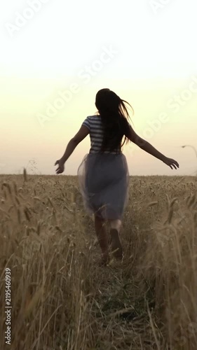 Young woman runs through golden wheat field at sunset, arms open, feeling free and happy.