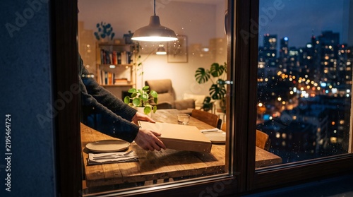 Delivery person placing pizza box on dining table in city apartment