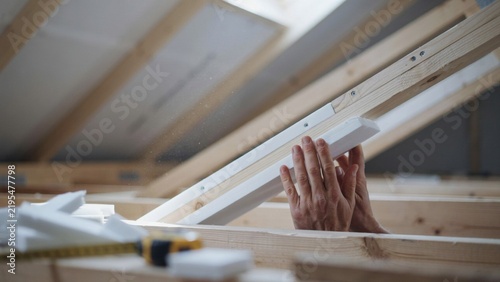 Worker hands installing white foam insulation panels inside roof frame.
