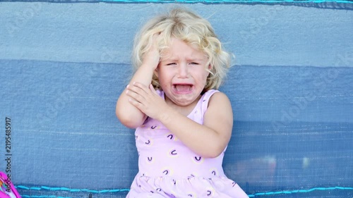 Little girl crying while sitting on a playground swing, slow motion. Emotional child expressing sadness outdoors on a playground. Childhood emotions and loneliness concept.