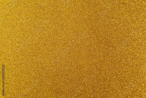 Macro texture of fine gold glitter surface with subtle shimmering particles. Seamless abstract background.