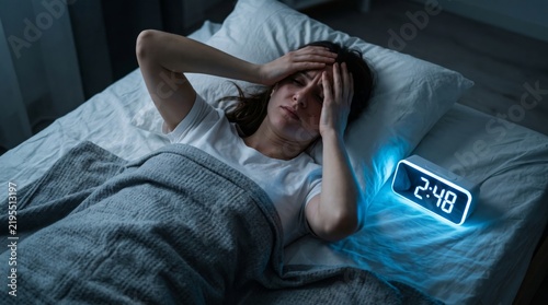 Stressed woman lying in bed awake at night looking at a digital clock showing 248 am, suffering from insomnia and sleep deprivation