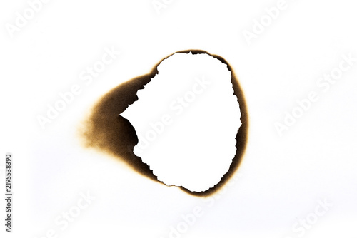 Irregular burnt hole in white paper with dark charred edges and smoke stains