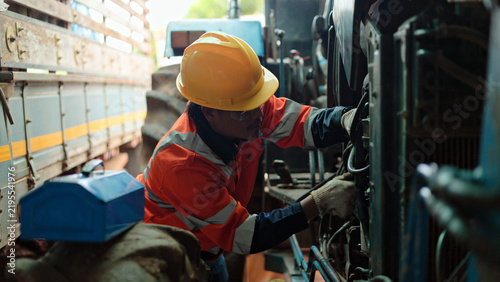 Professional mechanic inspecting and repairing engine of heavy agricultural tractor, farm equipment maintenance and repair service concept.