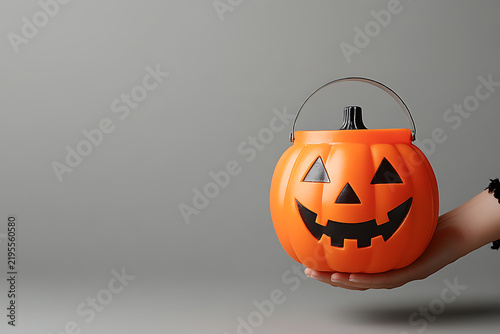 Clean minimalist shot of child hand holding jack-o-lantern bucket with huge blank space for spooky event advertising