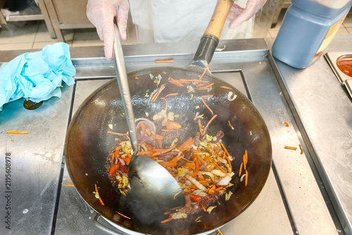 A cook prepares a vegetable mix in a hot frying pan.