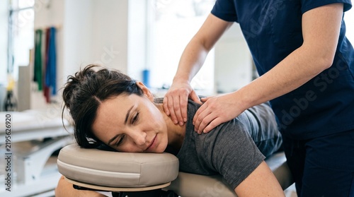 Physical therapist massages woman's neck and shoulders on a massage table in a clinic setting