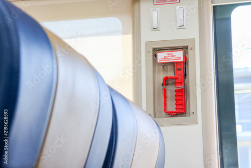 Red emergency handle visible inside train door. Clear plastic cover protects the device. Label warns passengers of its use. Bright red color draws attention. Found on public transport vehicles