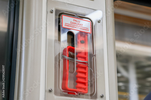 Red emergency handle visible inside train door. Clear plastic cover protects the device. Label warns passengers of its use. Bright red color draws attention. Found on public transport vehicles