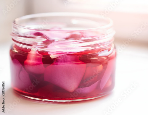 Pink rose petals macerated in clear glass jar with organic liquid extract for natural beauty and spa treatment herbal remedy product photography close up photo transparent filled bright