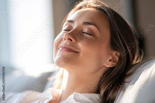 Close up of serene young woman relaxing with eyes closed enjoying sunlight indoors