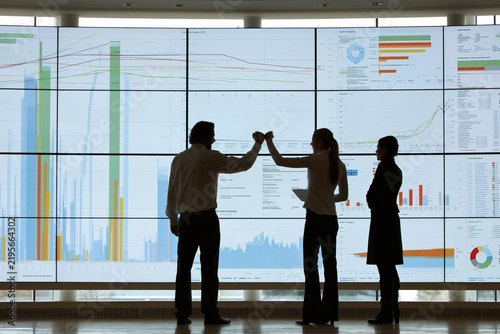 Silhouettes of business people celebrating success in front of a large digital data wall