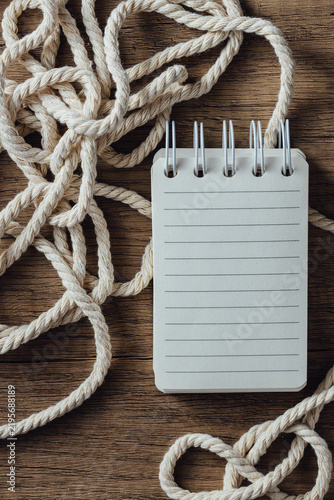 Foto Blank Notepad Surrounded by Twisted Rope on Wooden Surface
