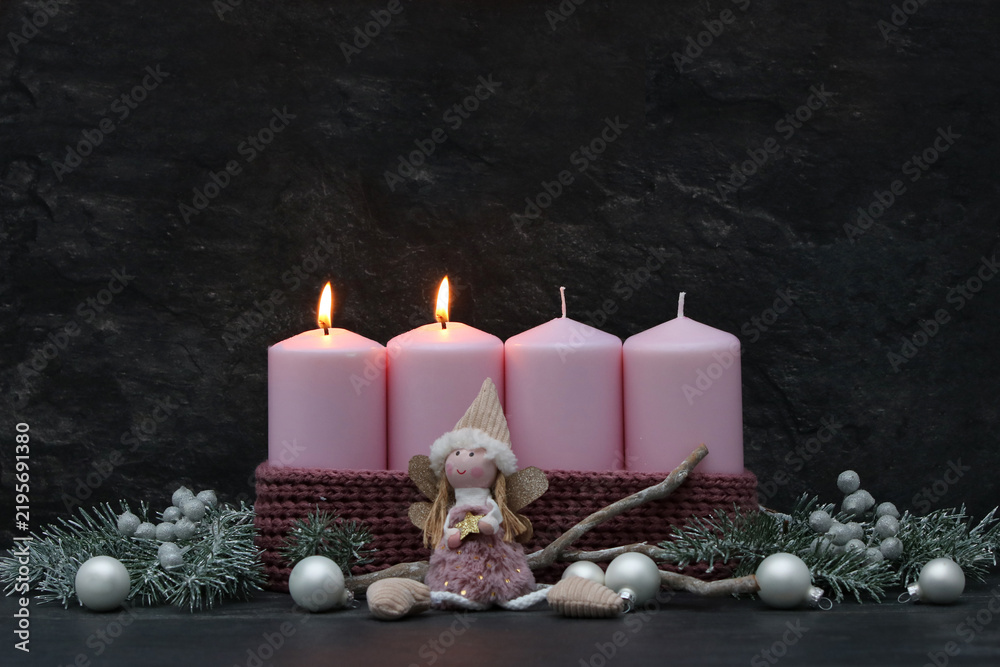 Fototapeta premium Second Sunday of Advent: Two burning pink candles on a modern Advent wreath featuring an angel figure, fir branches, and silver baubles against a dark background, with space for text.