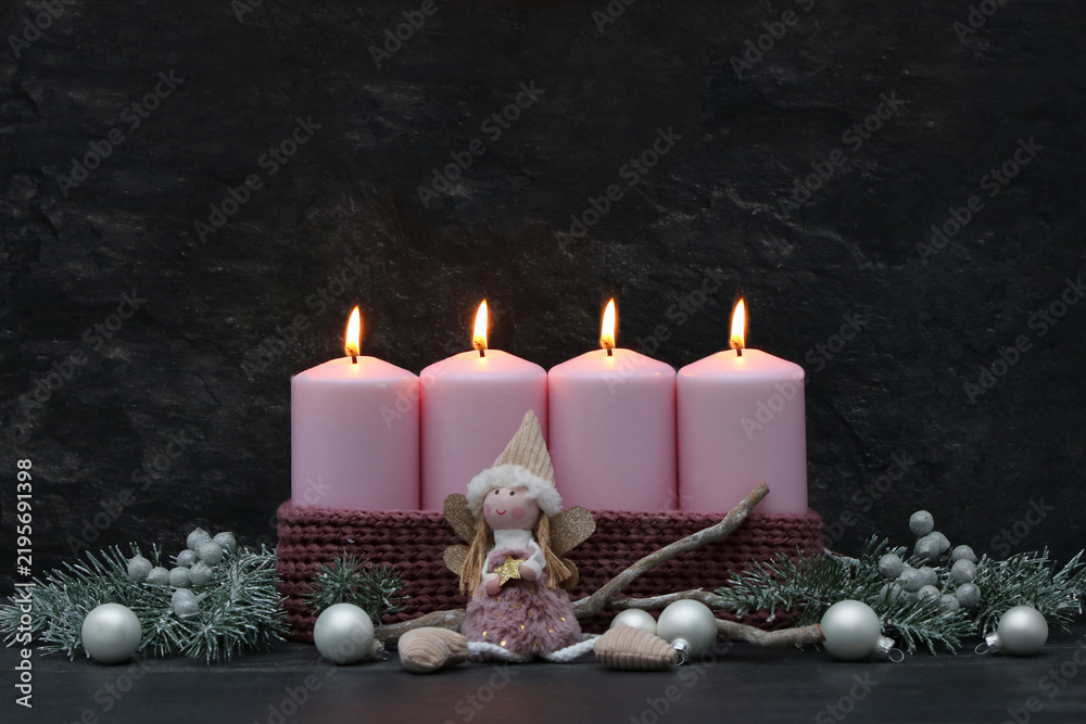 Fototapeta premium Fourth Sunday of Advent: Four burning pink candles on a modern Advent wreath with an angel figurine, fir branches, and silver baubles against a dark background, with space for text.