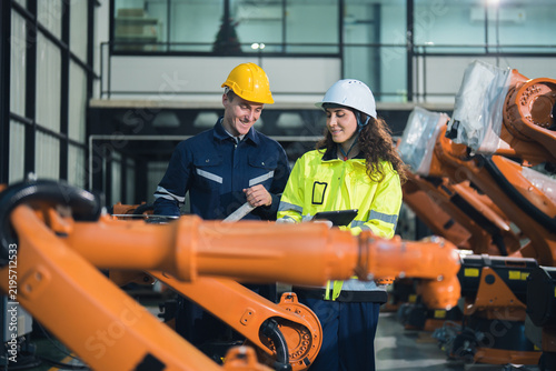 Factory technicians reviewing information on a tablet beside industrial robotic arms, manufacturing automation, digital inspection, collaborative monitoring, safety, and production efficiency