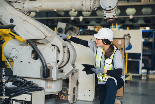 Factory technician inspecting an industrial robotic arm while using a tablet, preventive maintenance, equipment assessment, automation reliability, safety, and manufacturing operations