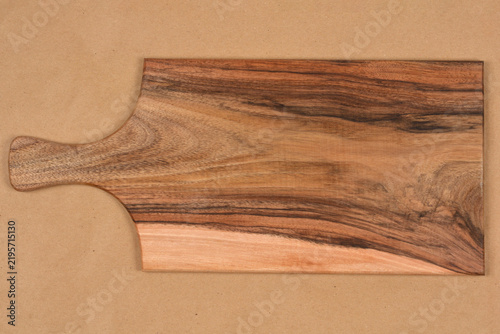 Fotografie A top view of a rectangular walnut wooden serving board with a distinct natural grain pattern and handle placed horizontally over a solid brown background