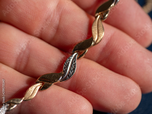 фотографія Macro close-up of a two-tone gold chain combining yellow and white gold leaf-shaped links, showing engraved texture and detailed jewelry craftsmanship in a hand